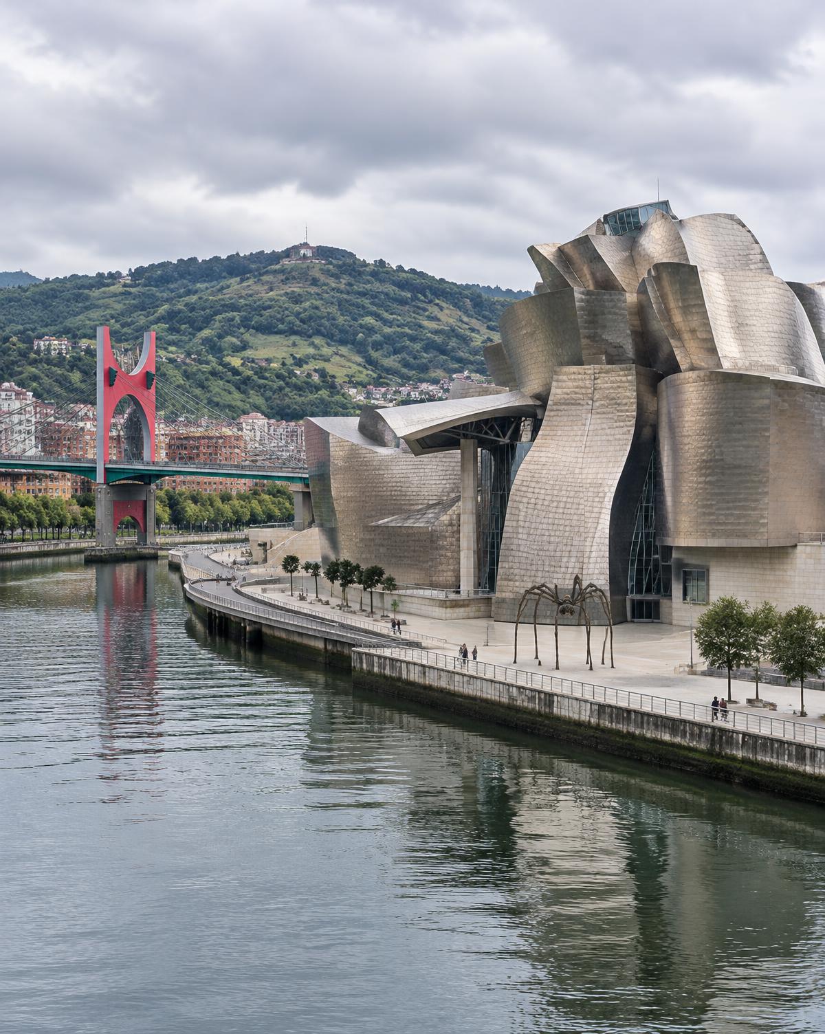 El museo Guggenheim de Bilbao junto a la ría, con el puente de La Salve y los montes al fondo