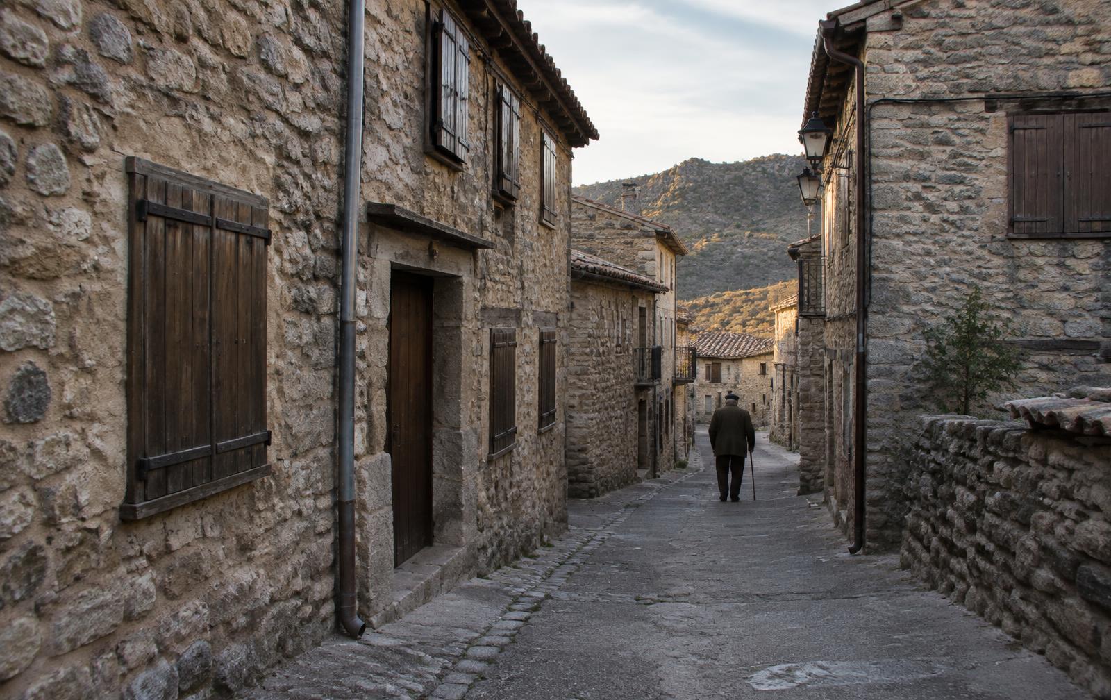 Calle de piedra vacía en un pueblo de montaña con un vecino caminando al fondo